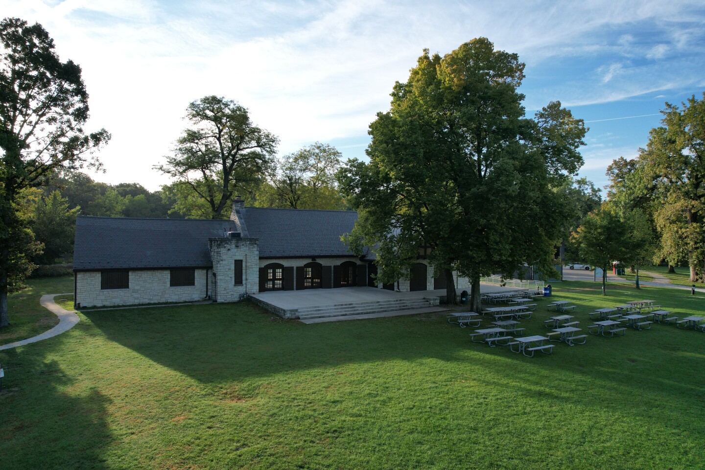 Image of trees, grass and a pavilion in front of a limestone building.
